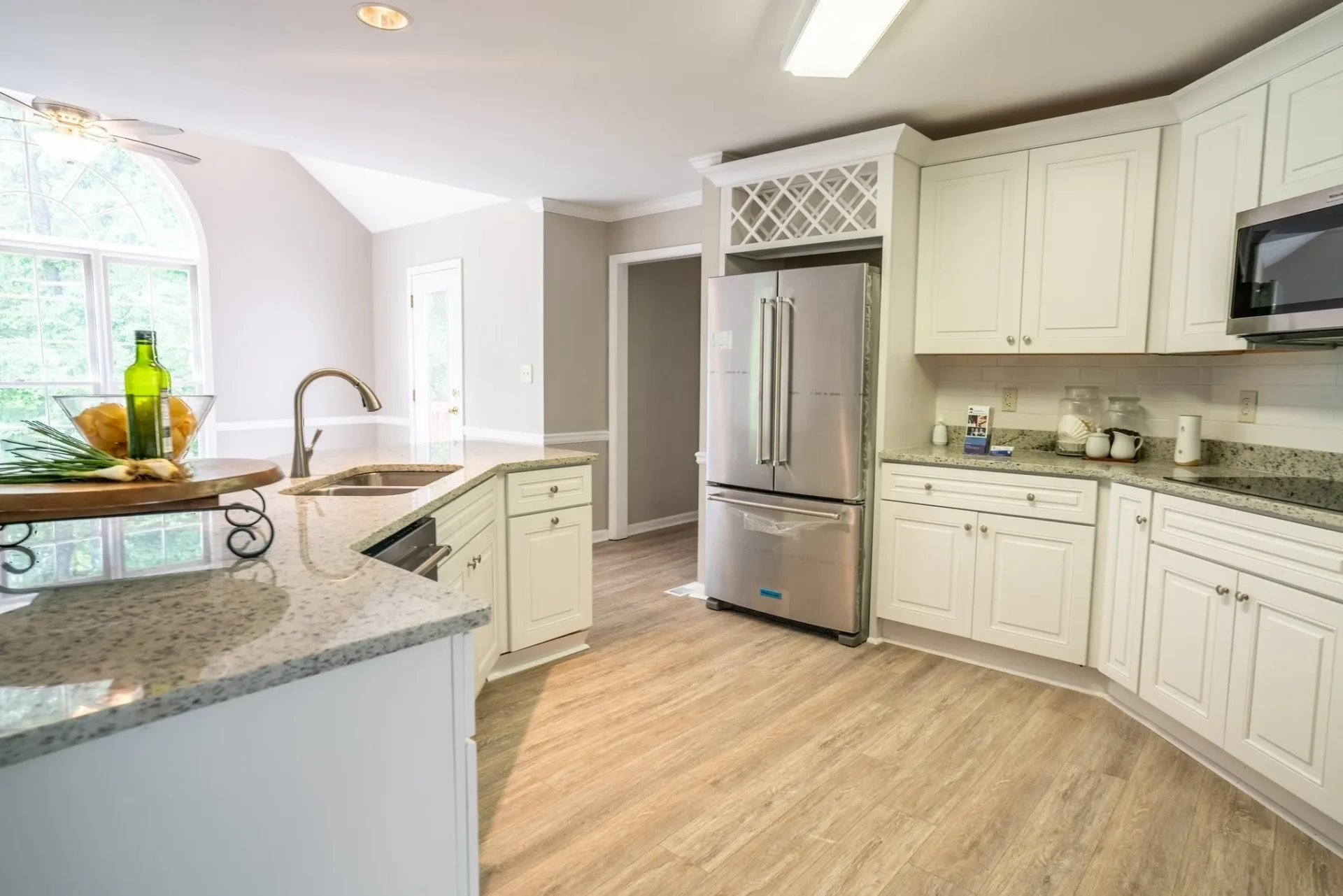 A kitchen with white cabinets and wood floors.