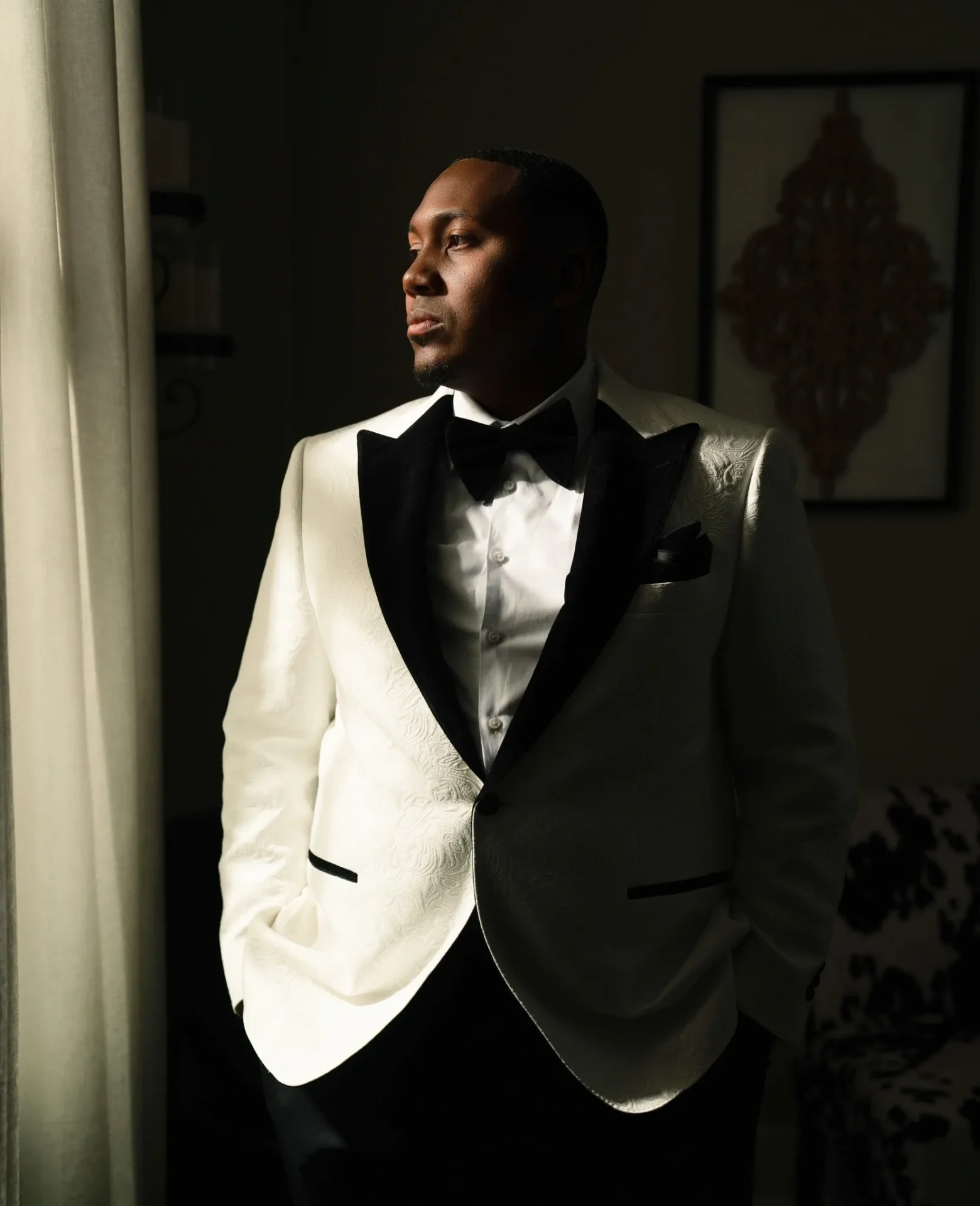 A man in a white tuxedo standing next to a window.