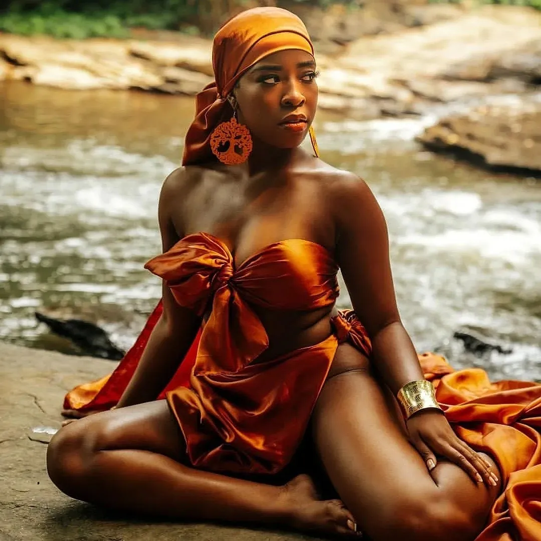 A woman sitting on the ground in front of a body of water.