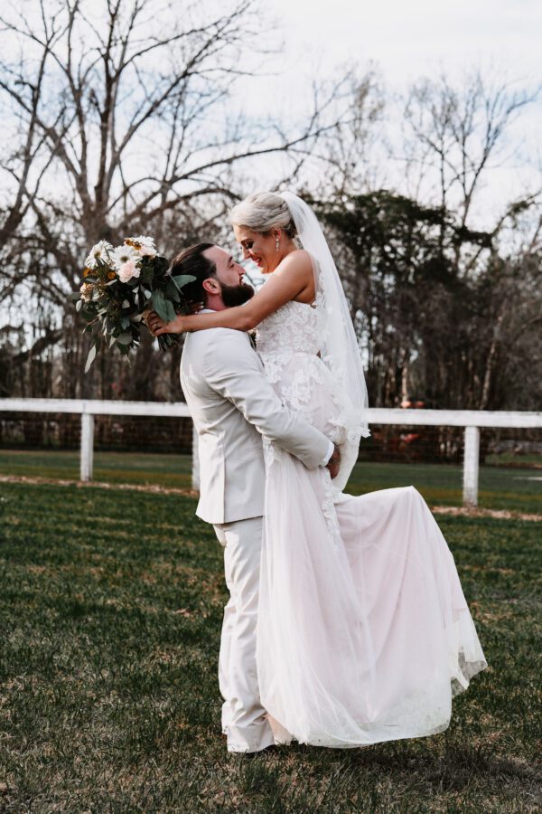 A bride and groom are hugging in the grass.