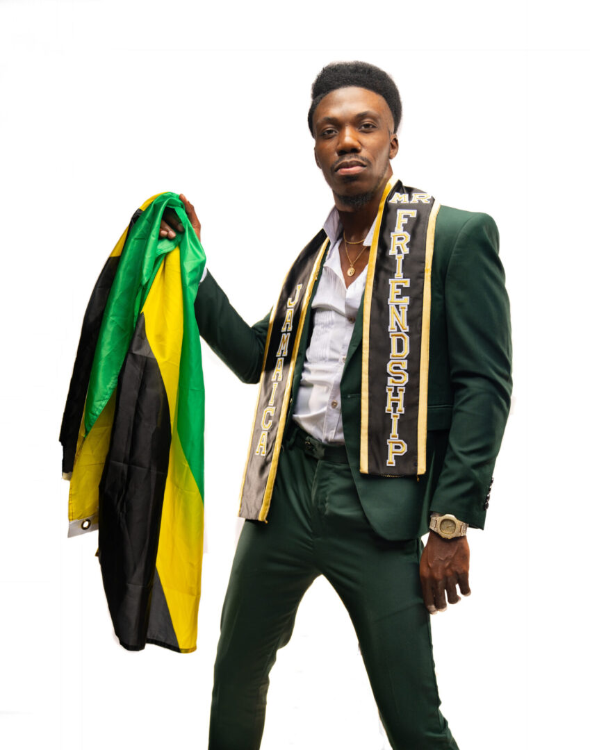 A man in green suit holding up a black and yellow scarf.