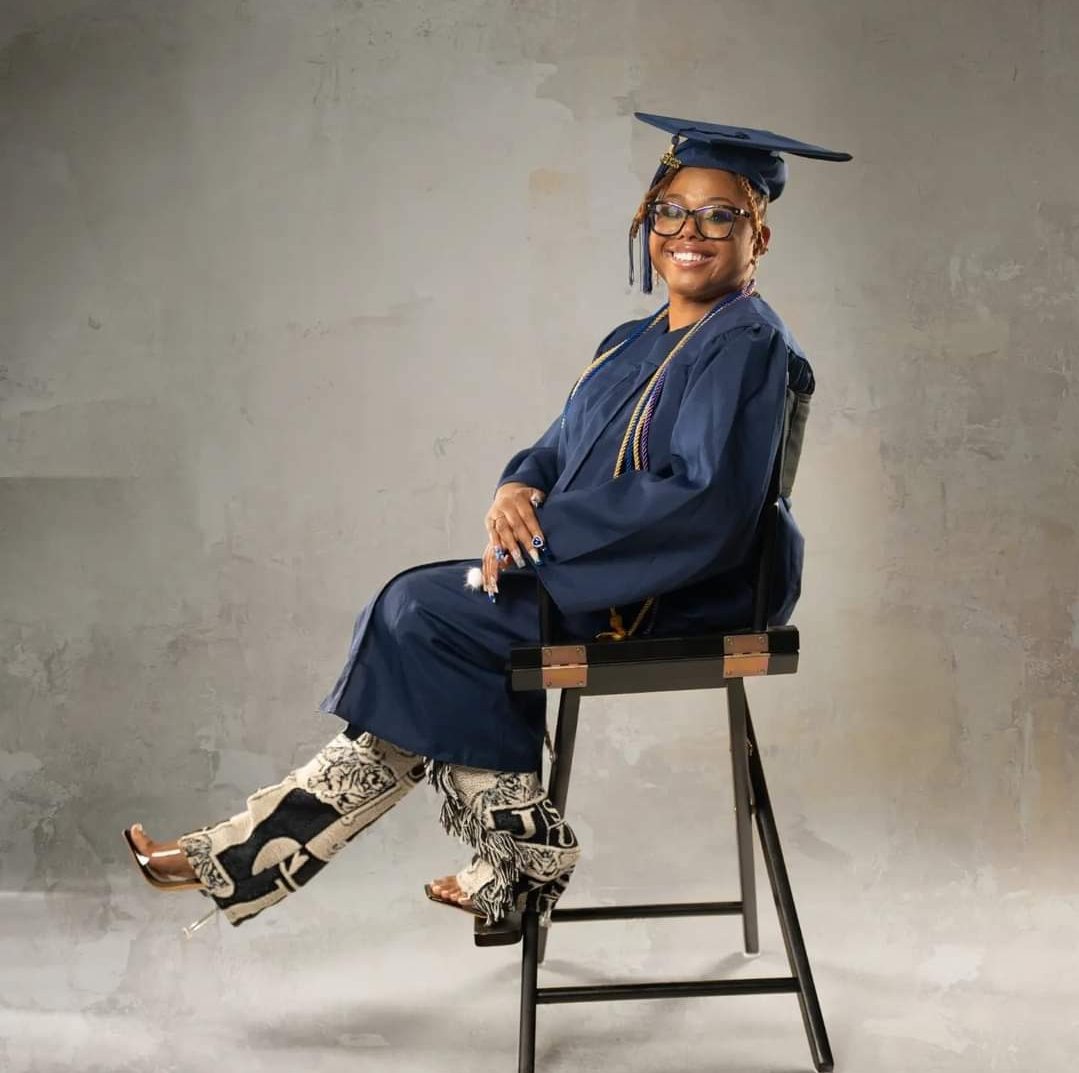 A woman sitting on top of a chair wearing a cap and gown.