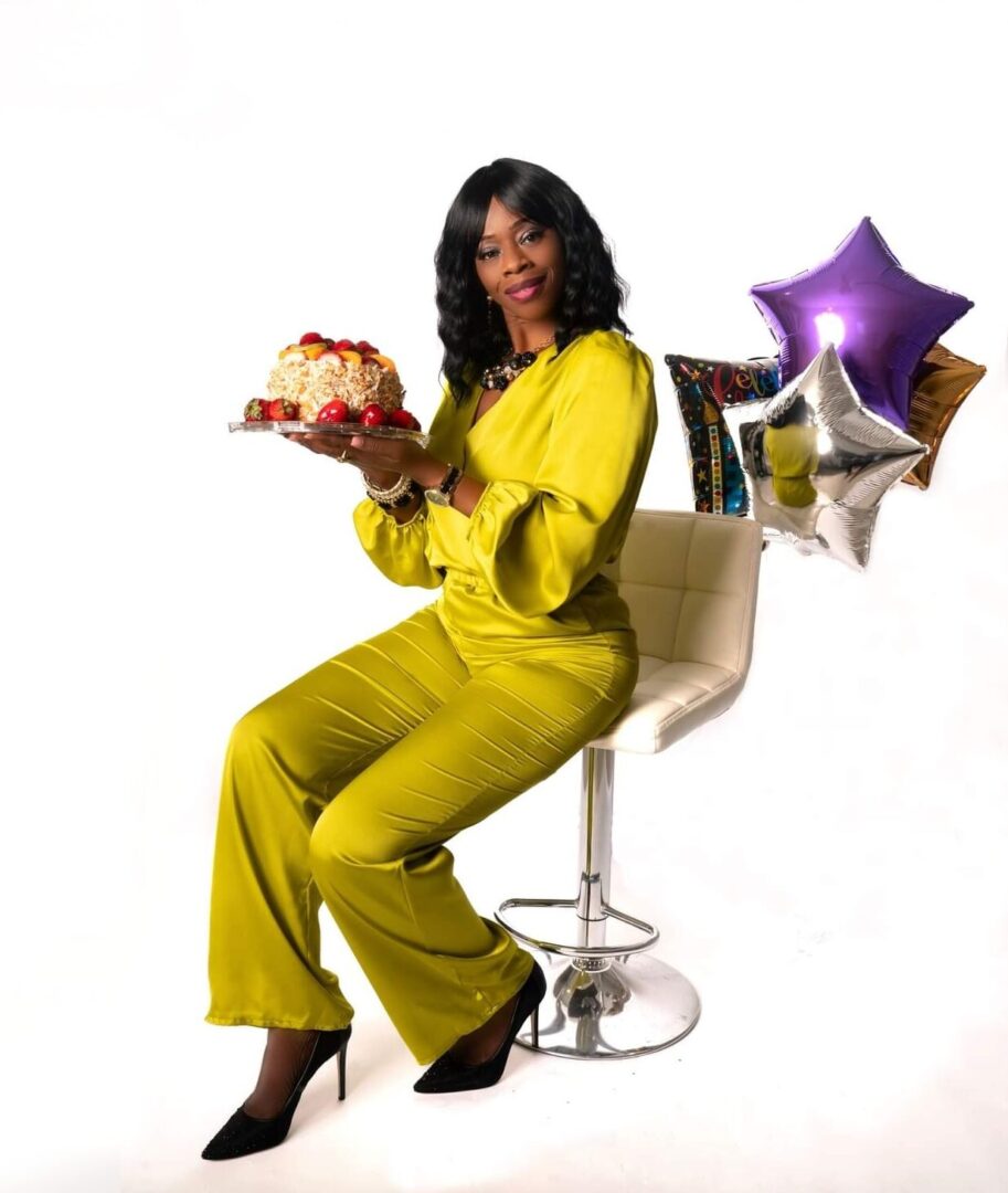 A woman in yellow sitting on a chair holding a cake.